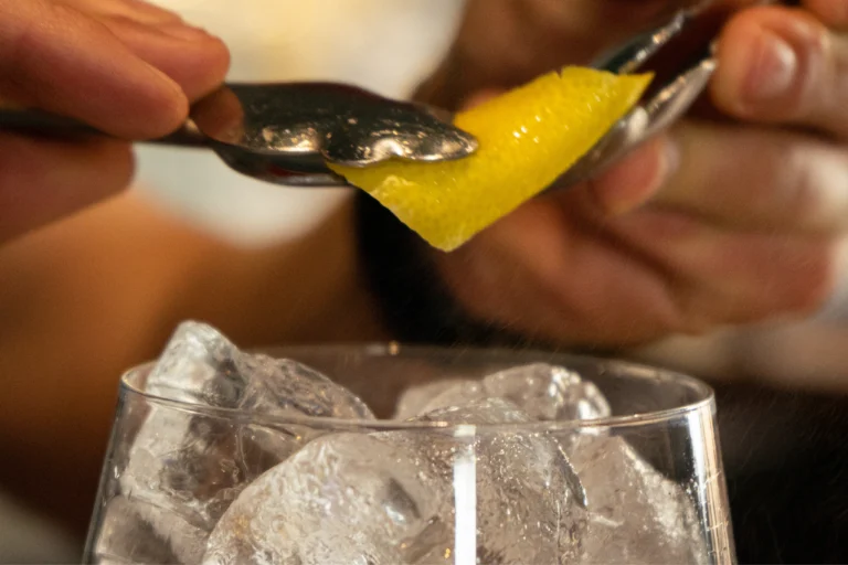 Preparación de cóctel con piel de limón en bar destino cuéllar café y copas.
